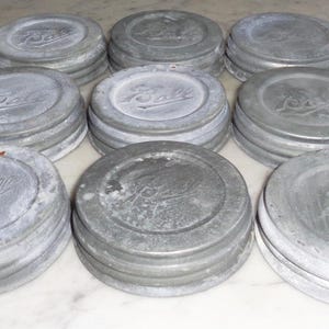 May include: Ten vintage silver-colored metal jar lids with the word "Ball" embossed on each lid.
