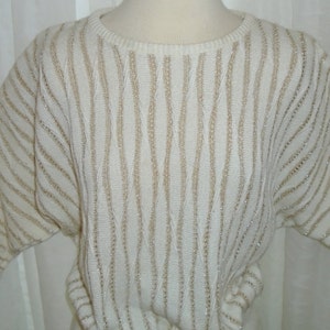 May include: A white sweater with gold stripes. The sweater has a round neckline and long sleeves.