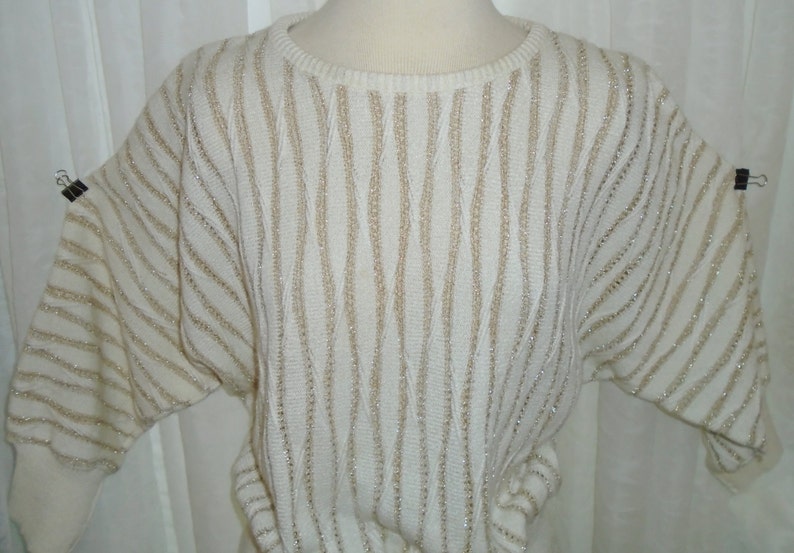May include: A white sweater with gold stripes. The sweater has a round neckline and long sleeves.