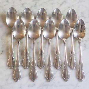 May include: A set of twelve silver spoons with ornate handles. The spoons are arranged in two rows of six, with the handles pointing towards the centre.