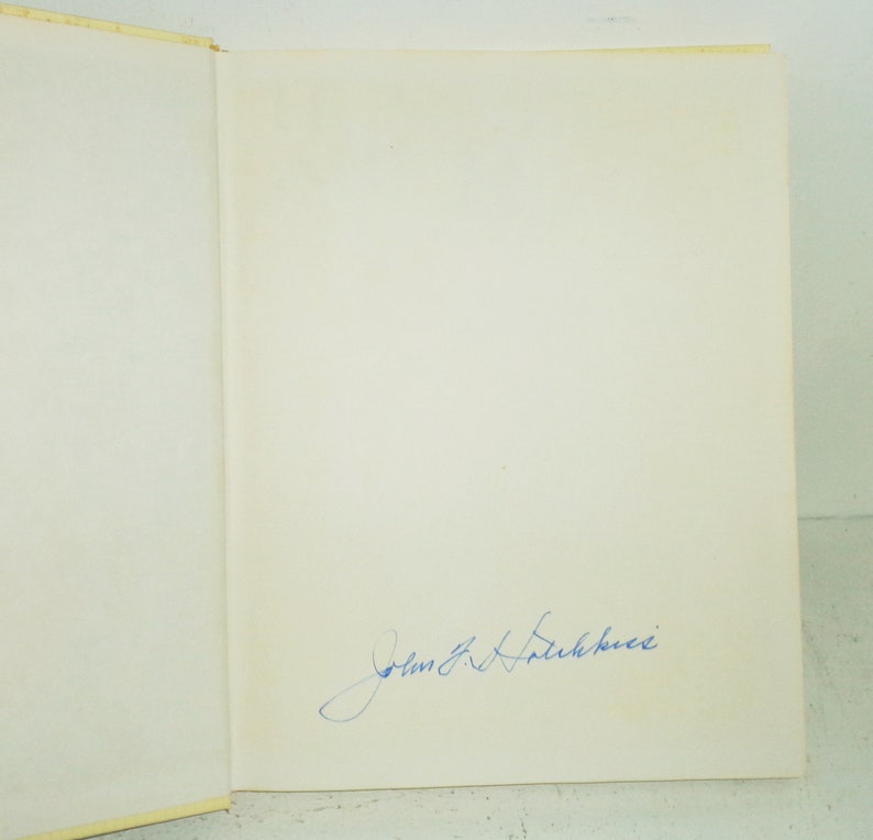 May include: A white book with a blue ink signature that reads "John R. Falkenberg".