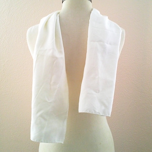 May include: A white scarf draped over a mannequin. The scarf is made of a soft, flowing fabric and hangs in a rectangular shape. The background is a neutral beige color.