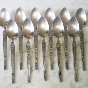 May include: Set of twelve silver spoons with an ornate floral design. The spoons have a heart-shaped design at the top of the handle.