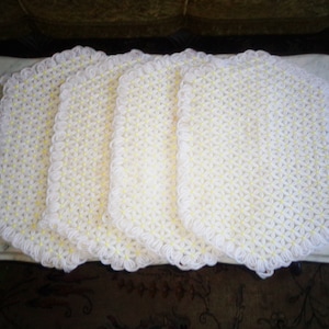 May include: Four white crocheted doilies with a daisy pattern and yellow centers. The doilies are arranged in a row on a white surface.
