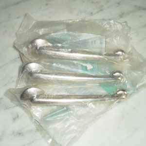 Könnte beinhalten: Drei silberne Türklinken, verpackt in durchsichtigen Plastiktüten. Die Griffe sind gebogen und haben eine glatte, polierte Oberfläche.