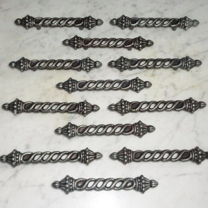 May include: Twelve silver-toned drawer pulls with a twisted design and decorative finials. The pulls are arranged in rows on a white surface.