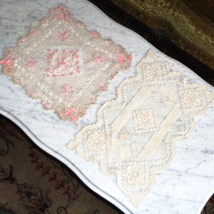 May include: Two delicate white lace doilies with intricate floral patterns. The doilies are on a white marble surface.