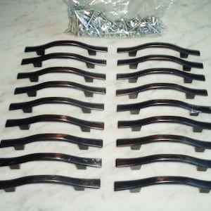 Puede incluir: Un juego de 16 tiradores de armario de níquel cepillado con un diseño curvo. Los tiradores están dispuestos en dos filas de ocho, y todos son del mismo tamaño y forma.