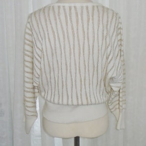 May include: A white sweater with a gold glitter stripe pattern. The sweater has a round neckline and long sleeves.