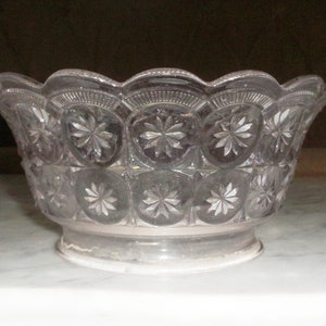 May include: A clear glass bowl with a scalloped rim and a starburst pattern. The bowl has a round base and is likely vintage. The bowl is made of clear glass and is likely used for serving.