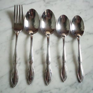 May include: Five pieces of silverware, including a fork and four spoons. The spoons are different sizes and are all made of shiny metal.
