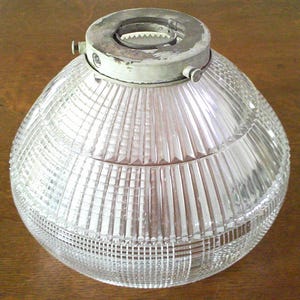 May include: A clear glass light shade with a spherical shape and vertical ribbed texture. The top features a circular metal fitter with three small screws for mounting. The glass surface has a repeating pattern of vertical lines and horizontal bands.