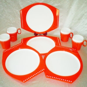 May include: A set of orange and white melamine dinnerware with a white snowflake design. The set includes four cups, two large plates, and two smaller plates.