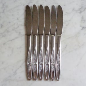 May include: Seven silver dinner knives with floral designs on the handles.