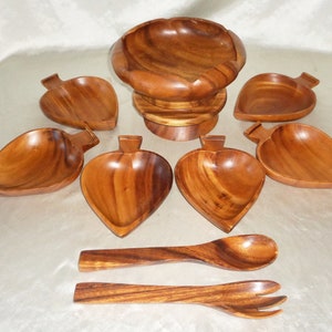 Pode incluir: Um conjunto de saladeira de madeira com uma tigela grande e seis tigelas menores em forma de folha. O conjunto também inclui dois utensílios de servir de madeira, uma colher e um garfo.
