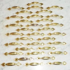 Puede incluir: Una colección de 24 pomos de armario dorados con un diseño en forma de corazón. Los pomos están dispuestos en filas sobre una superficie blanca.