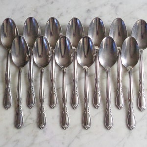 May include: A set of 15 silver teaspoons with ornate handles. The spoons are arranged in a row, with the handles pointing upwards.