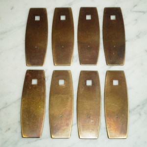 May include: Eight brass plates with a rectangular hole in the centre. The plates are slightly curved and have a worn, aged appearance.