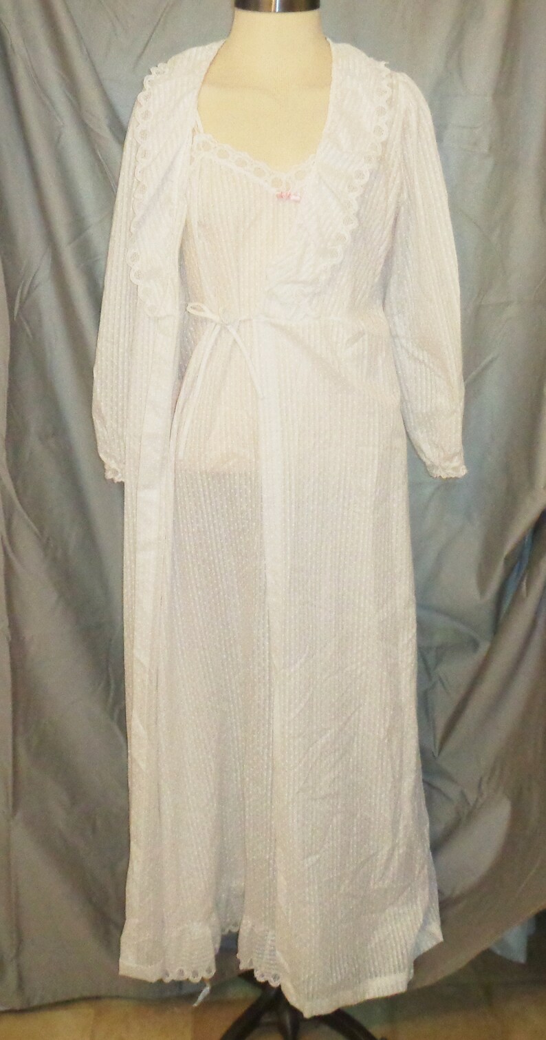 Puede incluir: Camis&oacute;n blanco de encaje con una bata a juego. El camis&oacute;n tiene un escote en V y un lazo en la cintura. La bata tiene mangas largas y un ribete de encaje.
