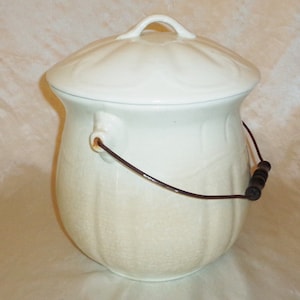 May include: White ceramic chamber pot with a lid and a wooden handle. The pot has a textured surface and a wire handle.