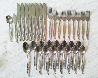 Puede incluir: Un juego de cubiertos vintage de acero inoxidable con cuchillos, tenedores y cucharas. Los utensilios tienen un diseño floral en los mangos. El juego incluye 16 cuchillos, 16 tenedores y 16 cucharas, ideal para una cena.