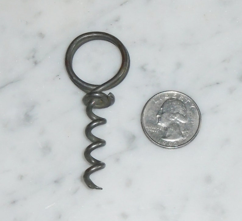 May include: A silver metal corkscrew with a loop handle. The corkscrew is about the size of a US quarter.