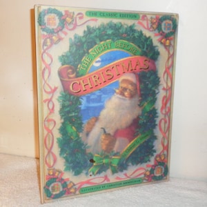 May include: The Classic Edition of "The Night Before Christmas" book cover features a colorful illustration of Santa Claus with a white beard and a red suit, holding a pipe. The cover is decorated with a green wreath, red ribbons, and gold bells.