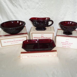 Könnte beinhalten: Eine Sammlung von rubinroten Glasserviceteilen aus der "1876 Cape Cod Collection". Das Set umfasst eine Servierschüssel, eine Sauciere, eine Bonbonschale und eine geteilte Servierschale, alle in ihren Originalverpackungen.