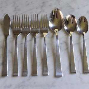 May include: A set of eight silver-toned flatware pieces, including a butter knife, four forks, and three spoons.