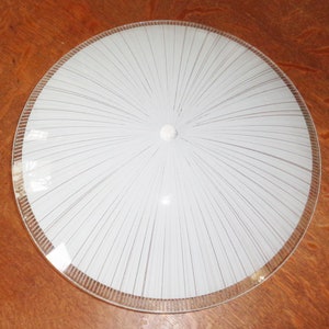 May include: A white glass ceiling light fitting with a clear glass rim and a radial pattern of lines radiating from the centre.