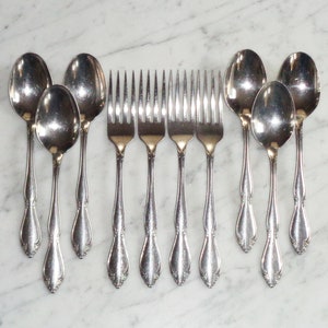 Puede incluir: Un juego de ocho cubiertos plateados, que incluye seis tenedores y dos cucharas. Los cubiertos tienen mangos adornados con un diseño decorativo.