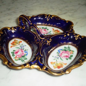 May include: A cobalt blue porcelain serving dish with three compartments. Each compartment has a gold rim and a floral design in the centre. The dish has a gold handle.