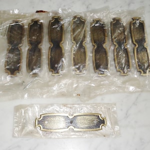 Puede incluir: Ocho tiradores de cajón de metal dorado con un borde decorativo y un acabado cepillado. Los tiradores están empaquetados en bolsas de plástico transparentes. Un tirador adicional se muestra por separado en una bolsa de plástico transparente.