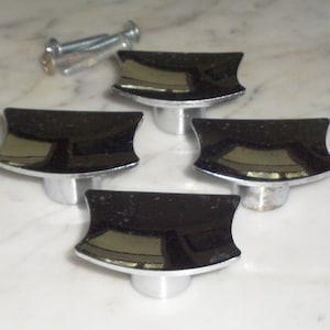 Könnte beinhalten: Vier verchromte Schrankknöpfe mit einer gebogenen, rechteckigen Form. Die Knöpfe haben eine glänzende, reflektierende Oberfläche.