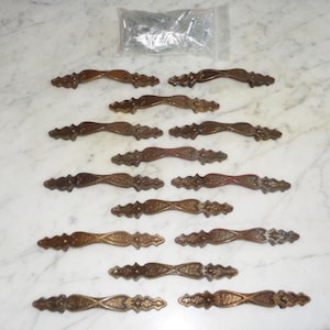 May include: A set of 10 ornate, gold-toned drawer pulls with a decorative design. The pulls are arranged in two rows of five, with the top row slightly offset from the bottom row.