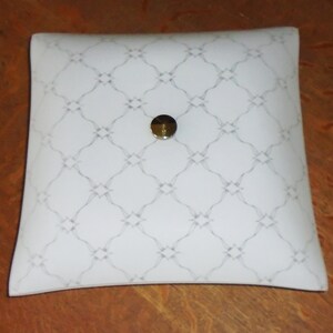 Può includere: Lampada da soffitto bianca con un paralume quadrato in vetro smerigliato, leggermente curvo. Il paralume presenta un motivo geometrico ripetitivo e un centro in metallo argentato.