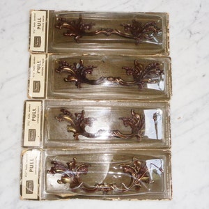 May include: Four packs of antique brass cabinet pulls with a floral design. Each pack is labelled "Sears" and "Pull" with the size "3 1/2" hole centre.
