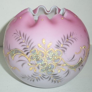 Könnte beinhalten: Eine runde, rosa Glasvase mit gerüschtem Rand. Die Vase ist mit goldenen und grauen floralen Designs verziert. Die Blumen haben eine hellblaue Mitte. Die Vase ist ein dekorativer Gegenstand.