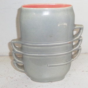 Peut inclure: Trois tasses en céramique grises empilées, chacune avec un design distinctif. Les tasses ont un corps arrondi, une anse et un intérieur de couleur corail contrastant. L'empilement met en valeur leur forme unique et le contraste des couleurs.