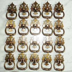 May include: Set of 18 antique brass drawer pulls with ornate designs. Each pull features a decorative, ornate, and intricate design with a ring handle.