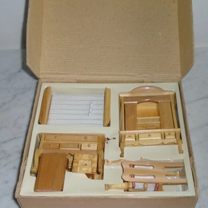 May include: A set of wooden dollhouse furniture in a cardboard box. The set includes a bed, a dresser, a wardrobe, and a chair. The furniture is made of unfinished wood and is ready to be painted or stained.