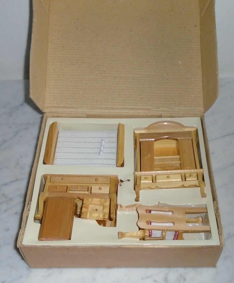 May include: A set of wooden dollhouse furniture in a cardboard box. The set includes a bed, a dresser, a wardrobe, and a chair. The furniture is made of unfinished wood and is ready to be painted or stained.