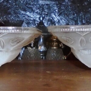 May include: Two white frosted glass bowls with a decorative pattern. The bowls are oval shaped and have a scalloped edge.