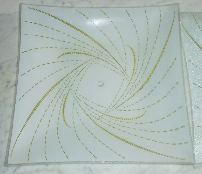 Pode incluir: Uma lumin&aacute;ria de teto quadrada branca com um padr&atilde;o de linhas douradas em espiral. As linhas s&atilde;o feitas de pequenos tra&ccedil;os e criam um efeito de espiral.