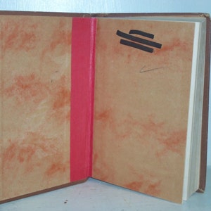 May include: A brown book with a red spine and a tan cover. The book is open to a blank page with a few black lines drawn on it.