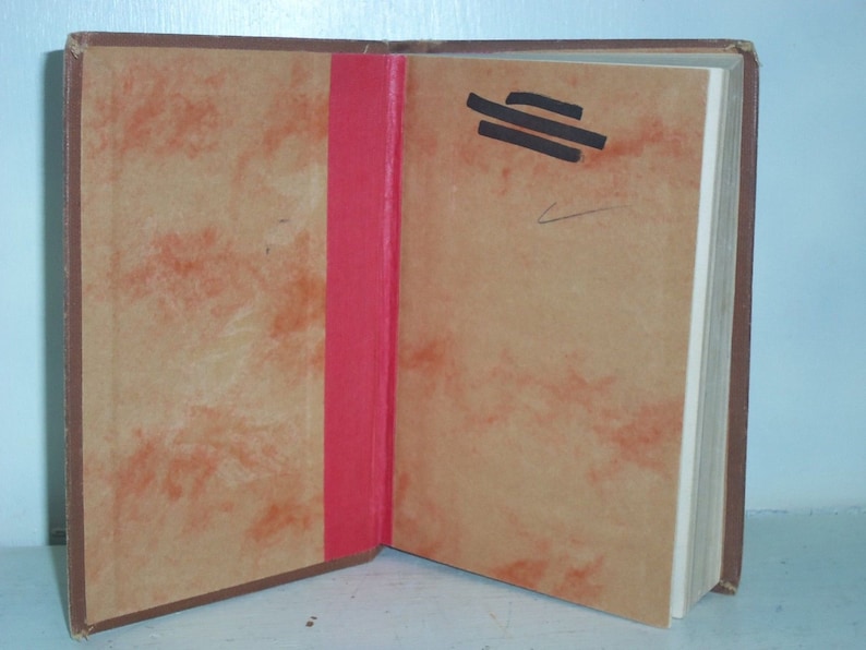 May include: A brown book with a red spine and a tan cover. The book is open to a blank page with a few black lines drawn on it.