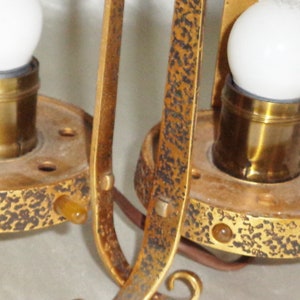 May include: Two gold-toned metal lamp fixtures with white light bulbs and decorative details. The fixtures have a textured surface and are attached to a ceiling or wall.