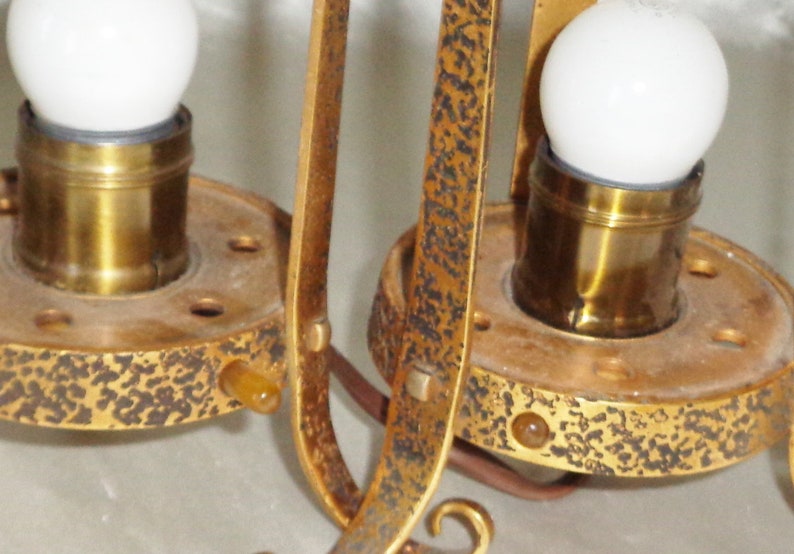 May include: Two gold-toned metal lamp fixtures with white light bulbs and decorative details. The fixtures have a textured surface and are attached to a ceiling or wall.