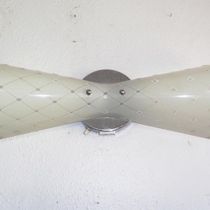 Puede incluir: Aplique de pared vintage de doble cono. La lámpara tiene una pantalla de color crema con un patrón de diamantes y pequeños acentos circulares. Está montada sobre una base circular de metal cepillado con dos tornillos pequeños.