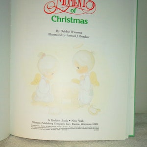 May include: A book cover with a green border. The cover features two angels with halos, praying. The title of the book is "Moments of Christmas" by Debbie Wiersma, illustrated by Samuel J. Butcher. The book is published by Western Publishing Company, Inc.